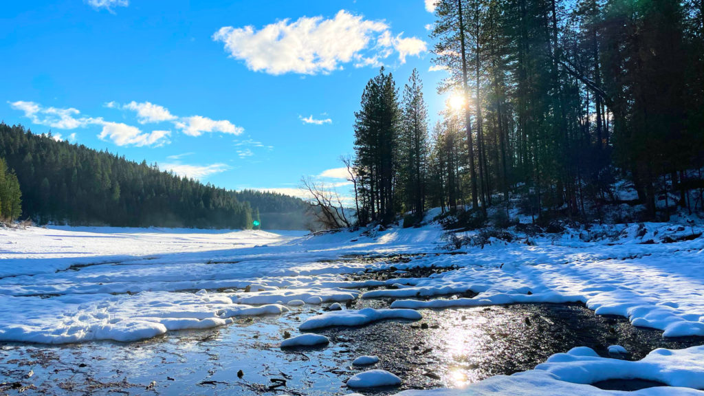 snowy hike by a river with the sun behind trees